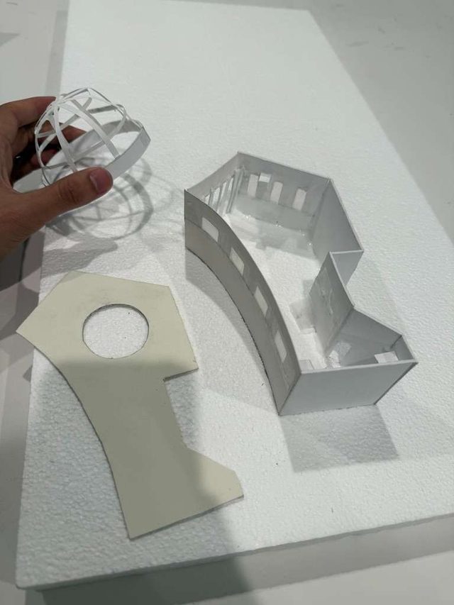 Hands assembling the curved white model walls and the perforated dome