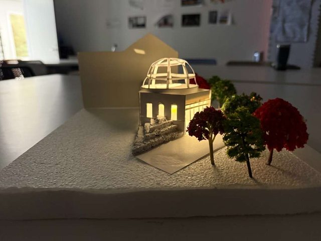 The model glowing from within, its lit dome surrounded by red and green trees