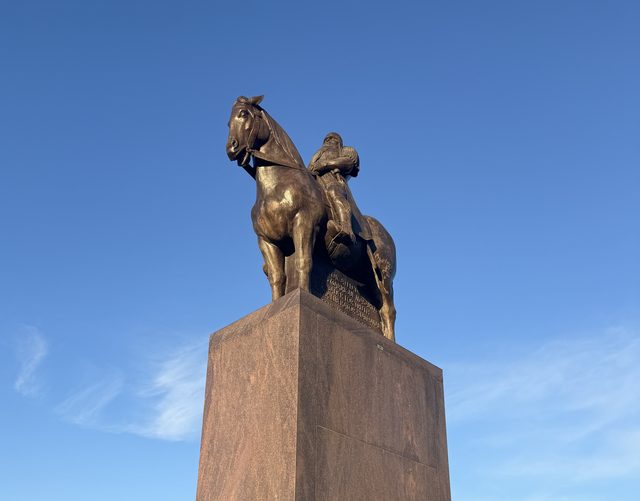 The existing bronze equestrian statue of T. G. Masaryk on its tall stone plinth against a clear blue sky