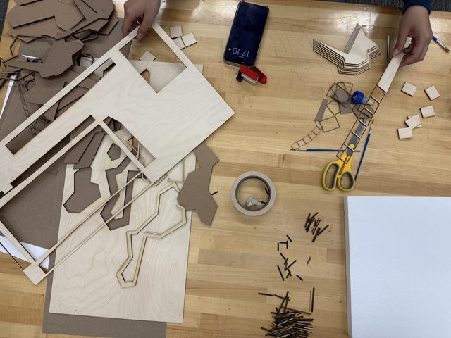 Laser-cut chipboard model pieces laid out on a workbench with cutting tools