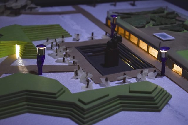 The model lit from within at dusk, seen from ground level across the terraces